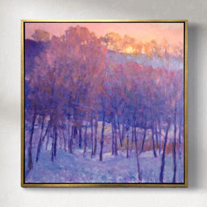 A painting of a snowy forest with a cool purple tone of the trees and the warm sun peaking behind the top framed in a gold floater frame hangs on a gallery wall.
