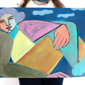 A woman holds a colorful painting of a woman on paper in front of a white wall. 