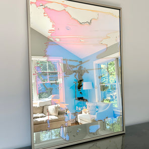 A fine art mirror rests on a dark dresser against a wall. 