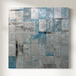 Abstract painting with metal patchwork of blue and gray squares hanging on a white wall.