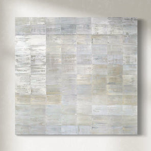 Abstract painting with a grid of rectangular panels in various shades of white, gray and gold hanging on a light gray wall.