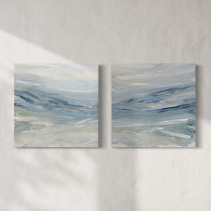 A pair of coastal paintings with blue, grey, white, cream, stone, teal, and yellow ochre paint hanging on a white wall by Teodora Guererra. 